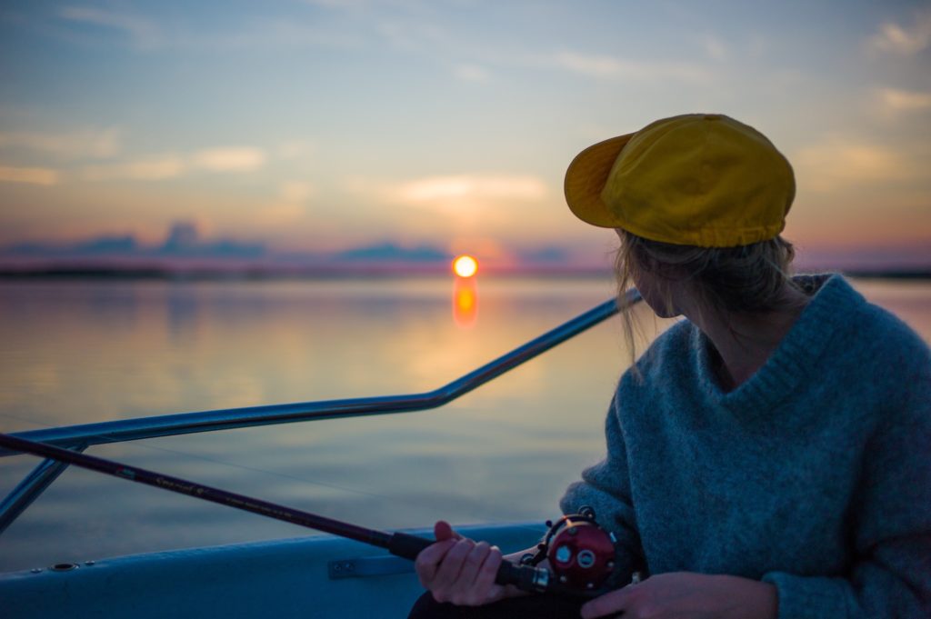 Woman fishing on a boat at sunset